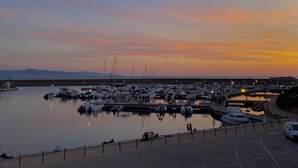 A marina with boats docked, a paved walkway, and a distant mountain range. - Libeccio | Relax Terrace 30m from the beach (Isola Rossa)