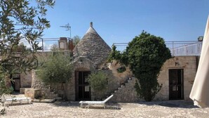Un patio con suelo de losas de piedra, un edificio de piedra con techo cónico y un árbol.