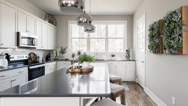 Een moderne keuken met witte kasten, een groot eiland, hangende lampen en uitzicht op de omgeving.