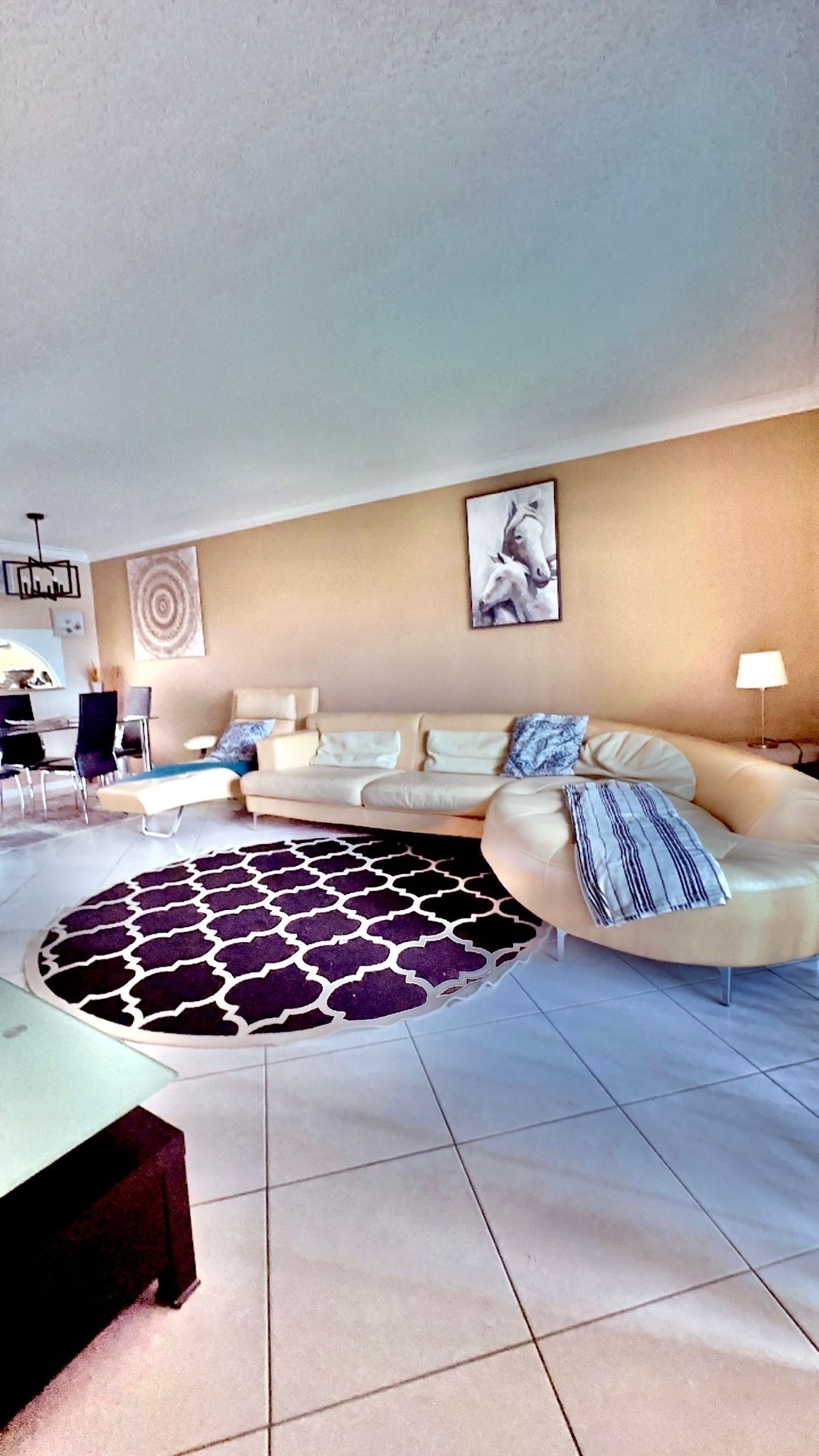En moderne stue med en beige sofa, et mønstret tæppe og et billede hængt på væggen.