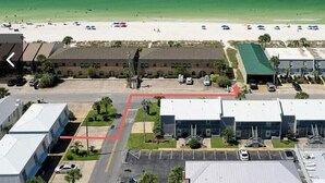 Vue aérienne d’une zone côtière avec une plage, des parkings et des bâtiments.