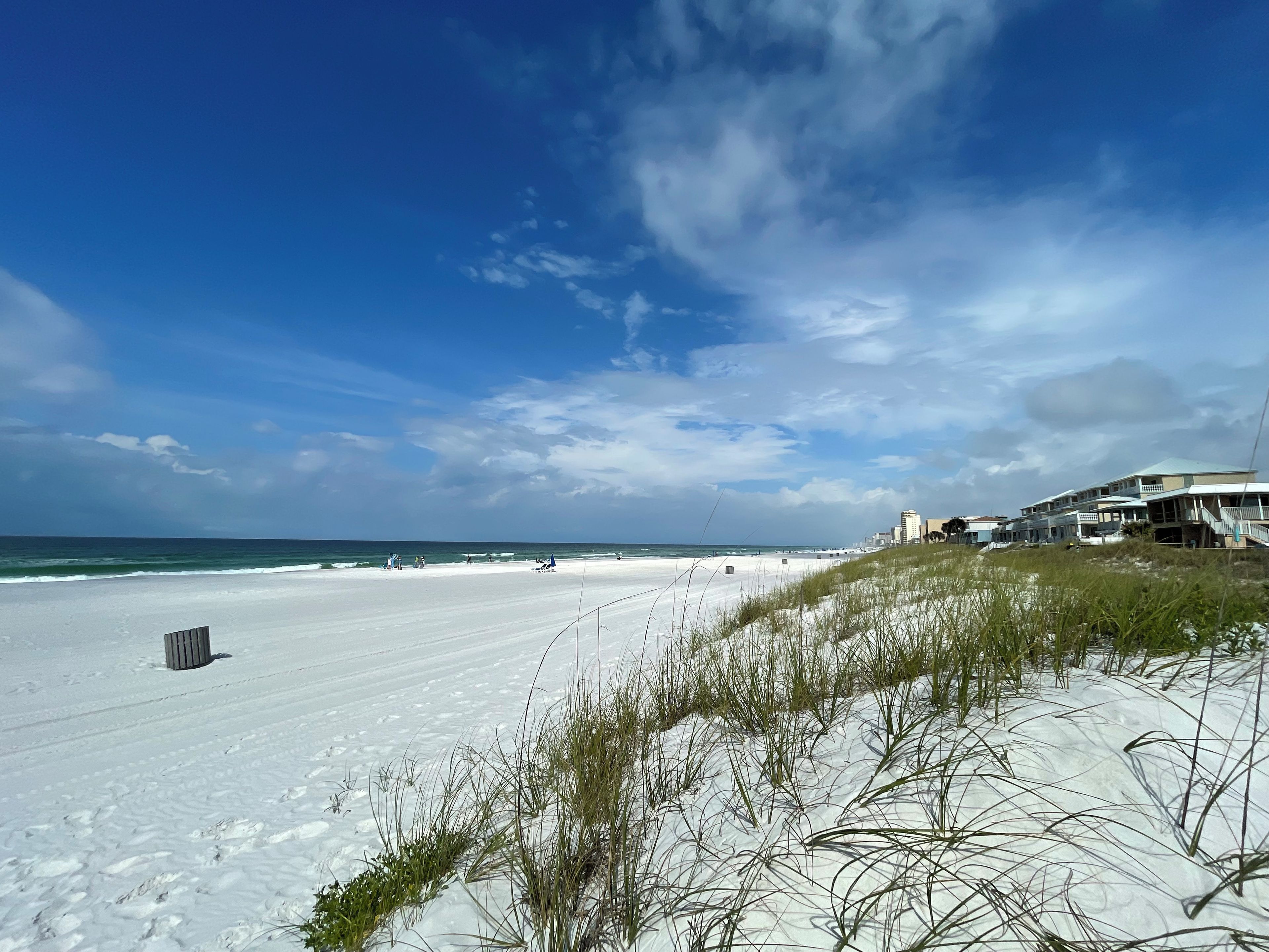 A beach with white sand, a clear sky, and buildings in the background.