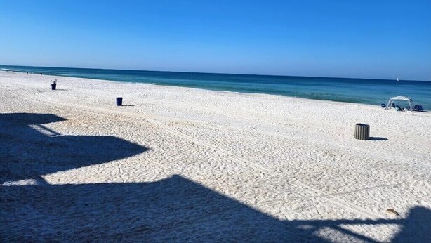 Une plage de sable blanc, avec une eau d’un bleu limpide, quelques chaises de plage et des parasols.