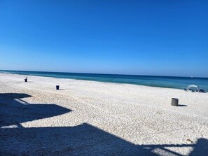 Une plage de sable blanc, avec une eau d’un bleu limpide, quelques chaises de plage et des parasols.