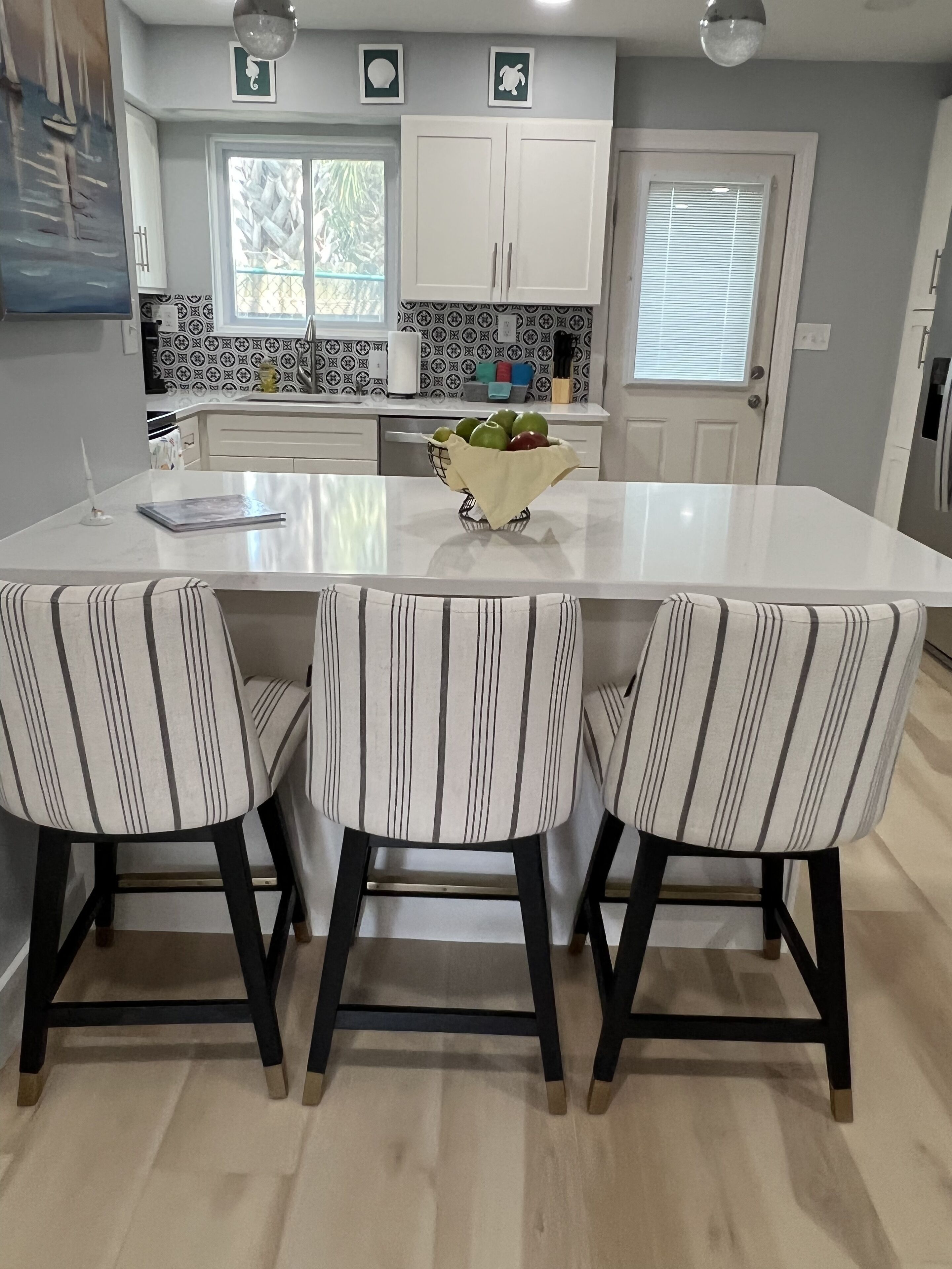 A kitchen with a central island, three striped chairs, and a fruit basket.