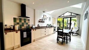 A modern kitchen with a dining area, featuring a central island, built-in appliances, and a large window providing natural light. - Charming 1 Bed Super Central  Terraced House (Cambridge)