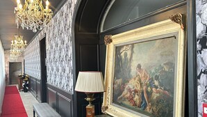 A hallway with a red carpet, a bench, a table with a painting, and a chandelier.
