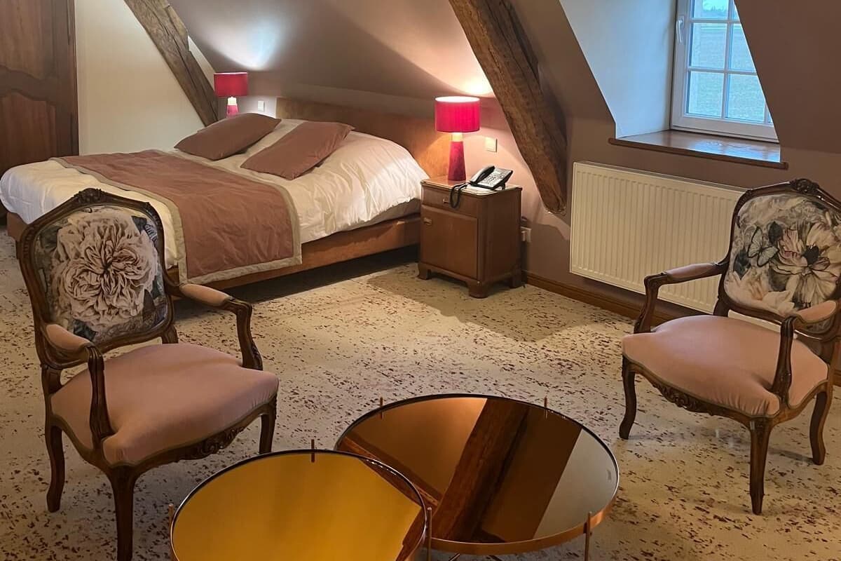 A bedroom with a large bed, two nightstands, a chair, a table, and a window.