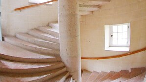 A spiral staircase in a building with white walls and two small windows.