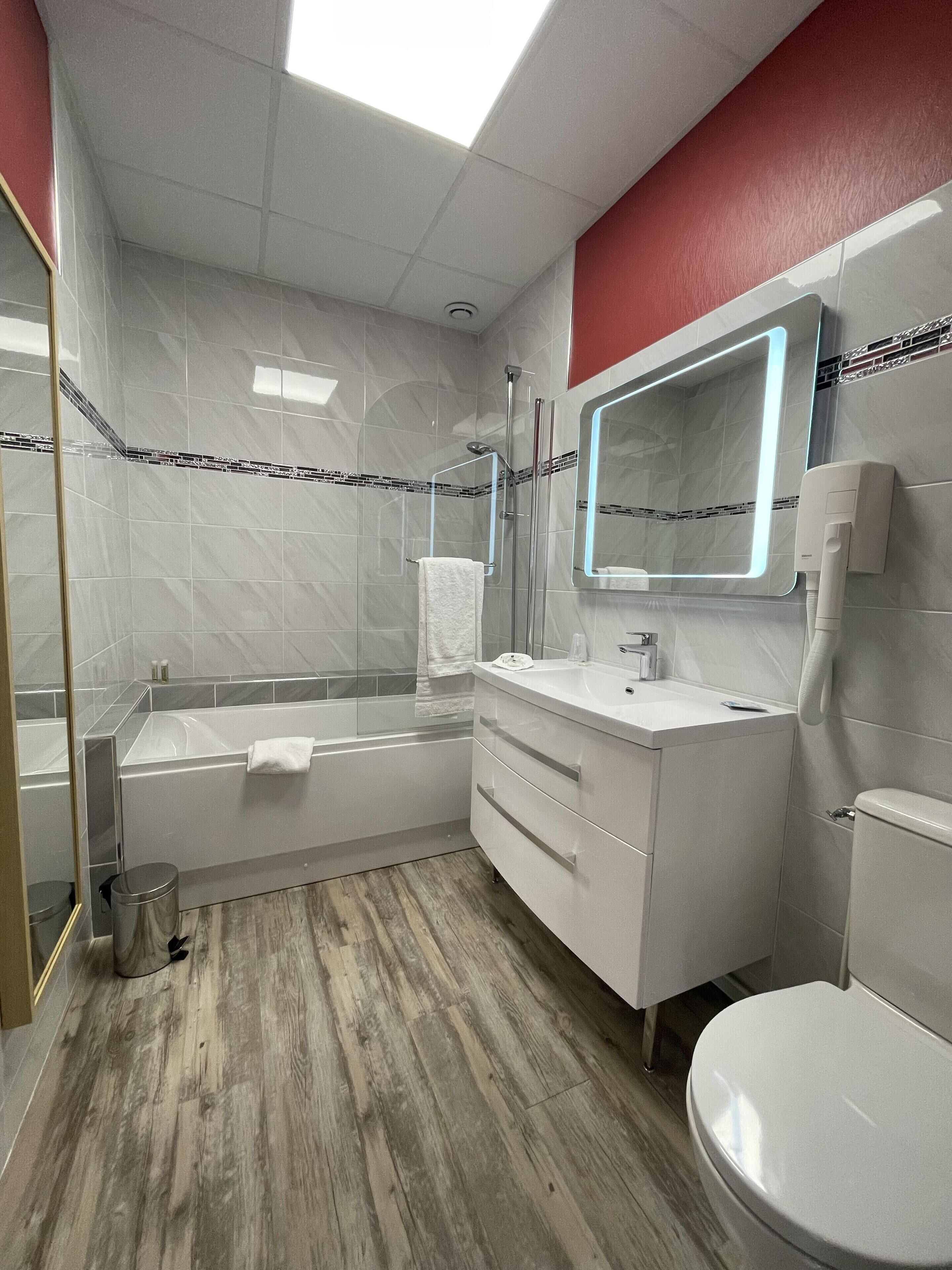 A modern bathroom with a bathtub, a vanity with a mirror, and a toilet.