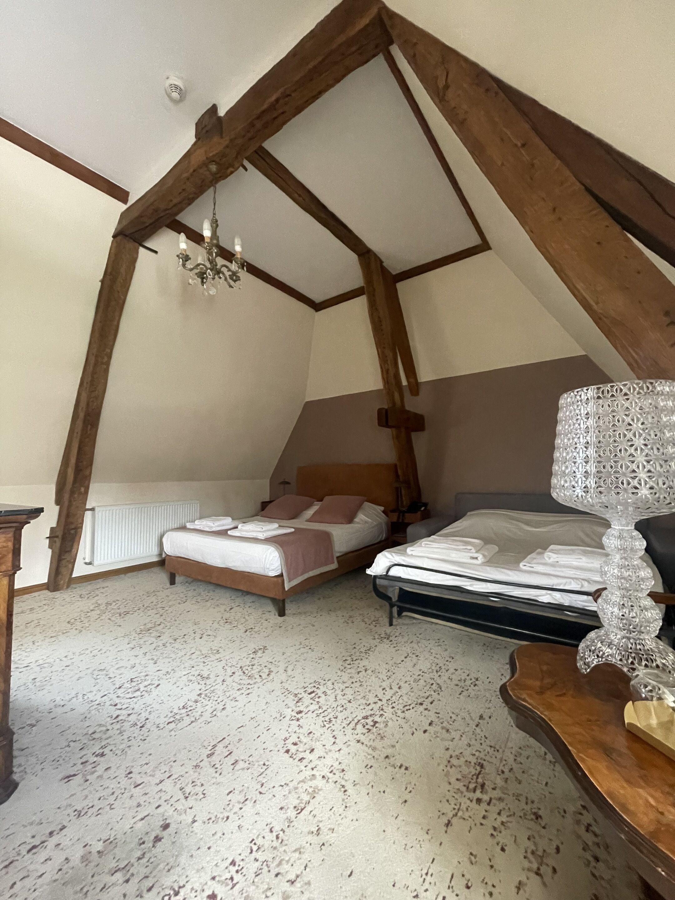 A bedroom with two beds, wooden beams, a chandelier, and a radiator.