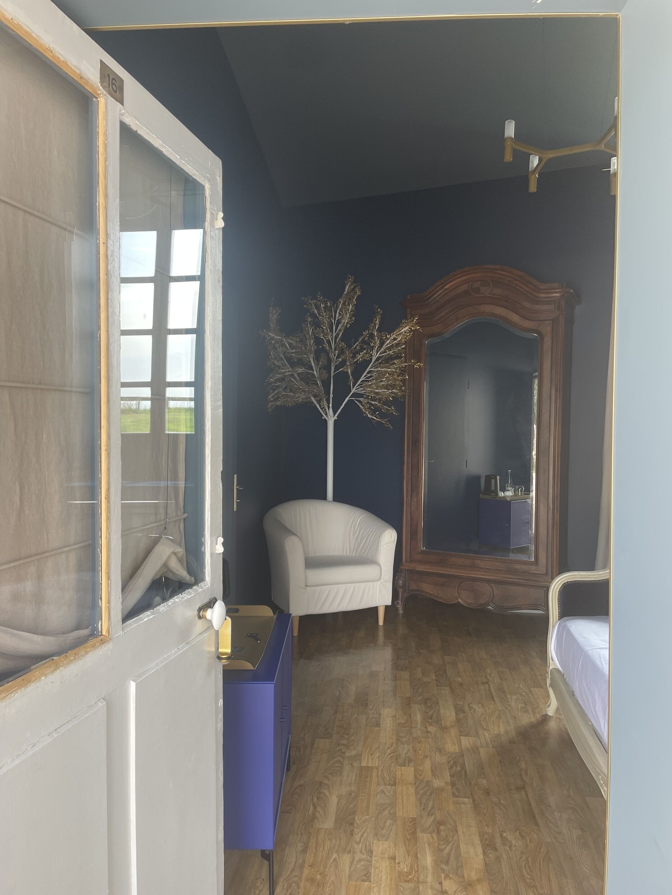Une chambre avec un plancher en bois, une chaise blanche, un grand miroir et un lit.