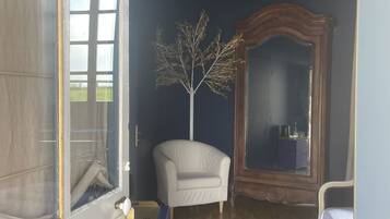 Une chambre avec un plancher en bois, une chaise blanche, un grand miroir et un lit.