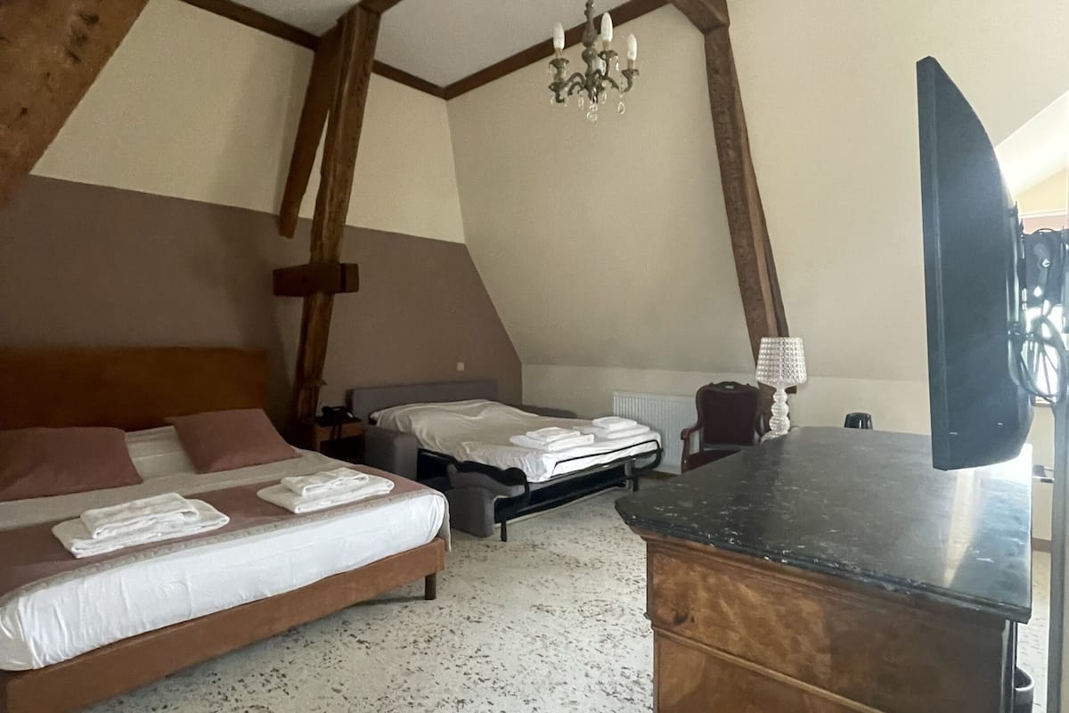 A bedroom with two beds, wooden beams, a chandelier, a flat-screen TV, and a wooden dresser.