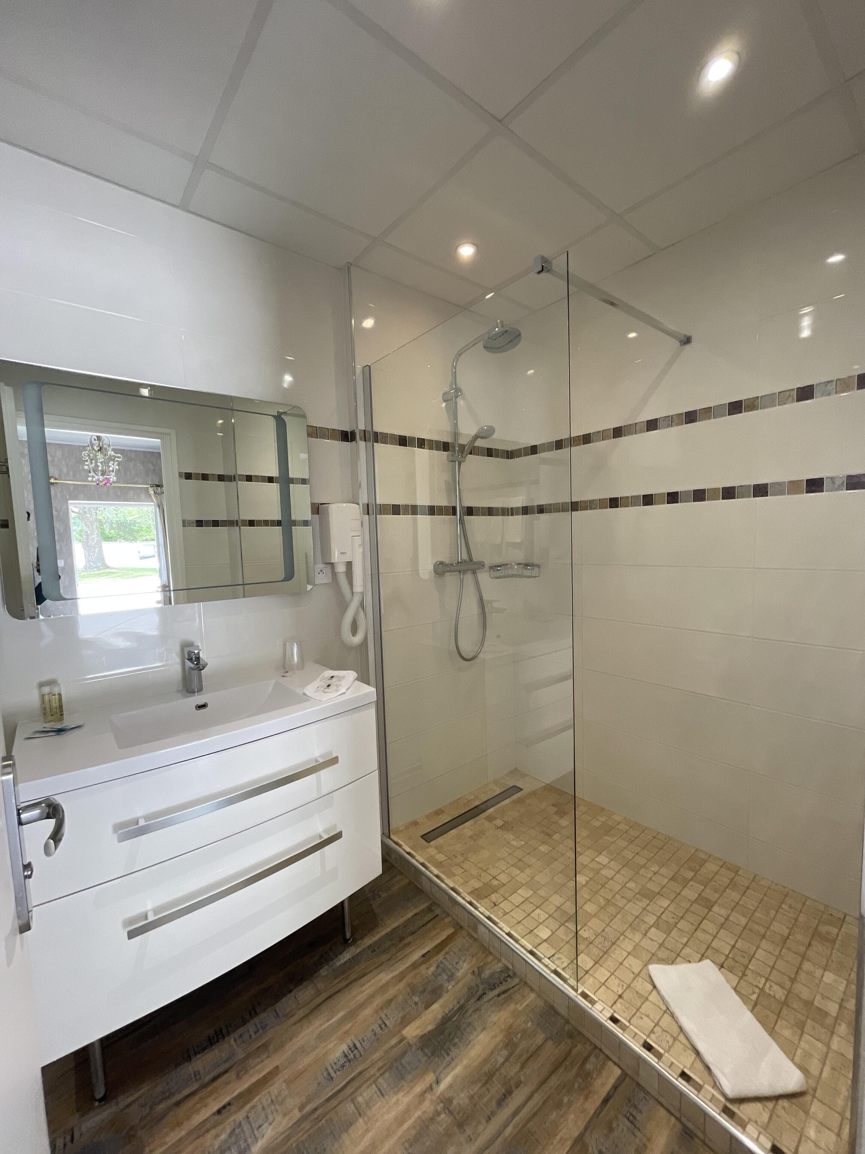 Un baño moderno con ducha envuelta en vidrio, un tocador blanco con cajones y suelo de baldosas.
