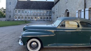 A vintage green car parked in front of a historic stone building with arched windows and a tower.