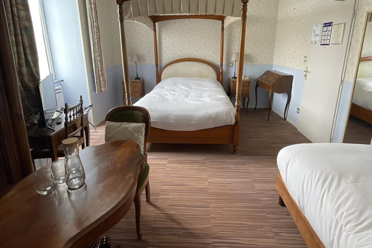 A room with a four-poster bed, a wooden desk with a chair, a small table, and a lamp.