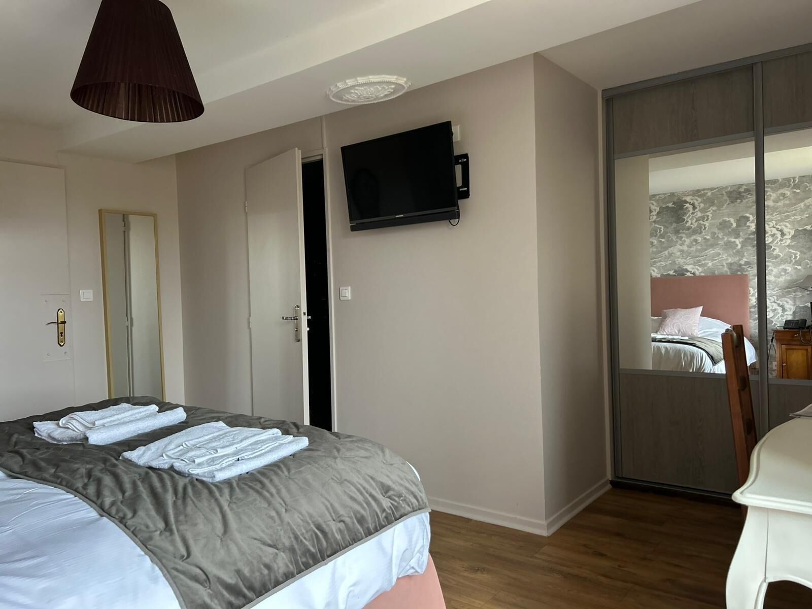A bedroom with a bed, a TV mounted on the wall, a door, and a view of a balcony with a bed and a chair.