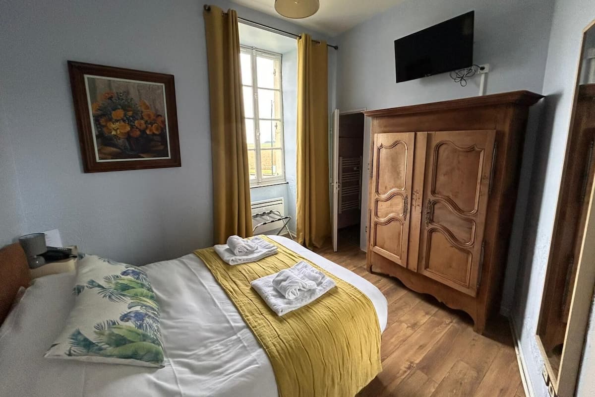 A bedroom with a bed, a painting, a wardrobe, and a television.