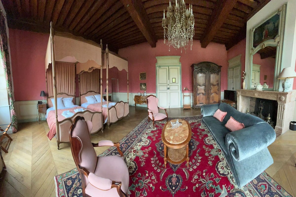 A room with a four-poster bed, a sofa, a chair, a small table, and a fireplace.
