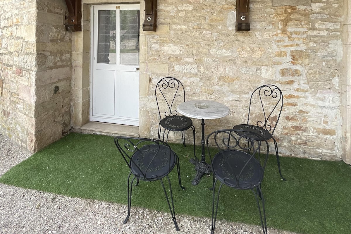 A stone building with a wooden balcony, a white door, and a small round table with four chairs.