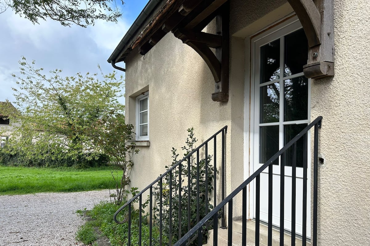 A building with a stone facade, a wooden staircase, and a gravel driveway.