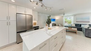 Una cocina moderna con una isla central, electrodomésticos de acero inoxidable y un comedor con sofá y mesa de centro.