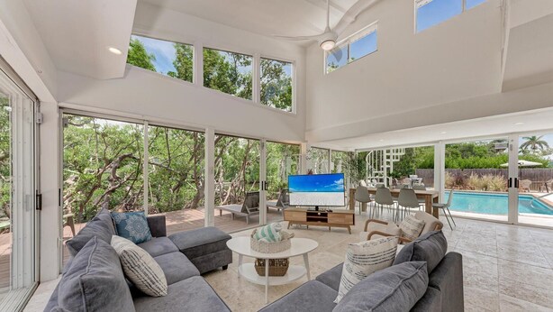 Amplia sala de estar con un sofá seccional gris grande, televisor de pantalla plana y comedor con vista a la piscina.