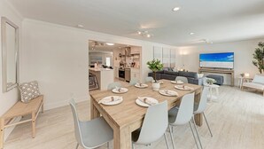 Una sala de estar moderna con un televisor grande, un comedor con una mesa y sillas de madera, y una cocina al fondo.
