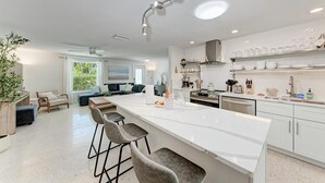 Una cocina moderna con una isla central, taburetes de bar y un comedor con sofá y sillas.