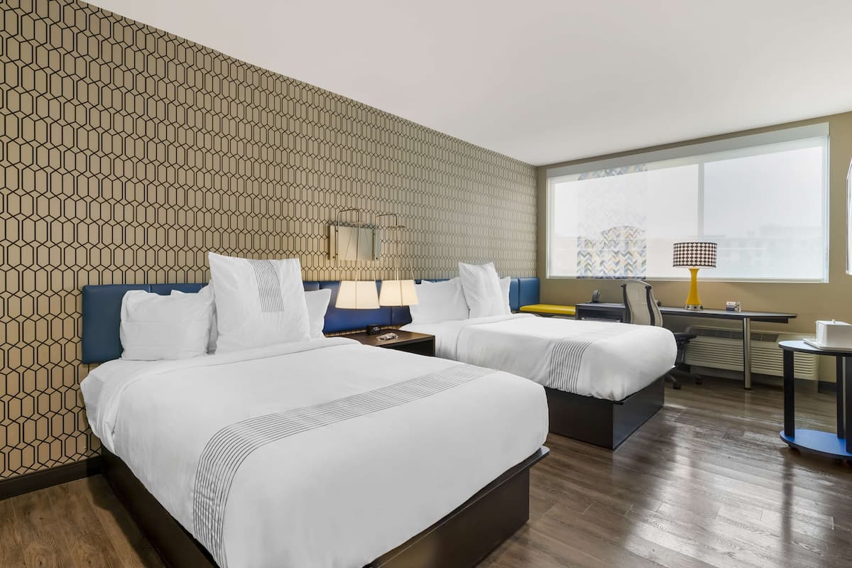 Une chambre d’hôtel avec deux lits, un bureau, une chaise et une fenêtre donnant sur un paysage agréable.