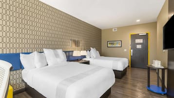 A hotel room with two beds, a desk, a chair, a TV, and a patterned wall.