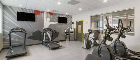 A gym with treadmills, elliptical machines, and a mirrored wall.