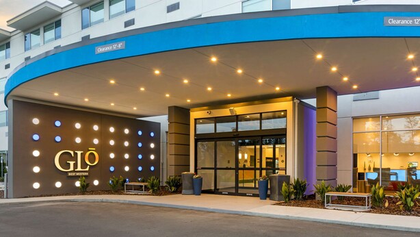 Ein Hotel mit blauem Markisenvorbau, beleuchteter Beschilderung und einem offenen Eingangsbereich.
