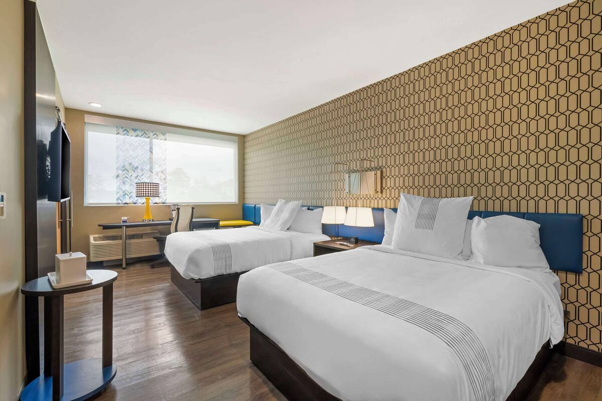 Une chambre d’hôtel avec deux lits, un bureau, une chaise, une télévision et une fenêtre donnant sur un beau paysage.