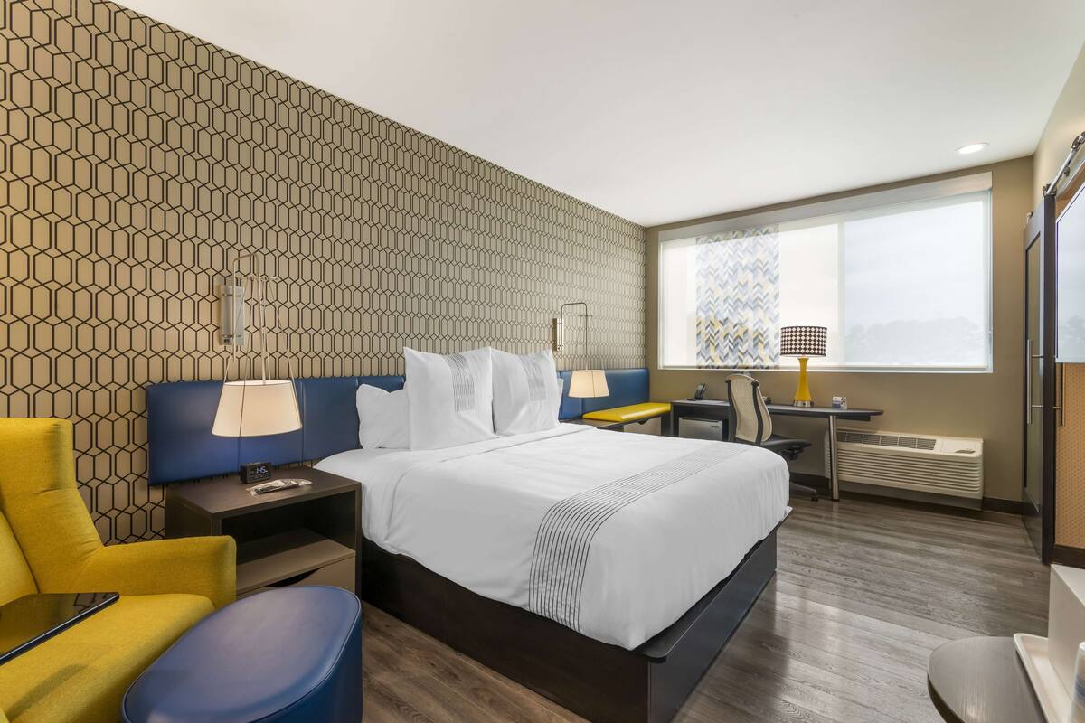 Une chambre d’hôtel avec un lit, un bureau, une chaise et une fenêtre donnant sur un paysage agréable.