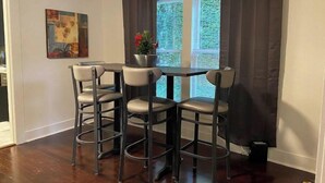 A dining area with a round table and four bar stools. There is a potted plant on the table and a painting on the wall. - Tyler's Texas Rose, a beautiful 2BR/1BA house with back yard (Tyler)