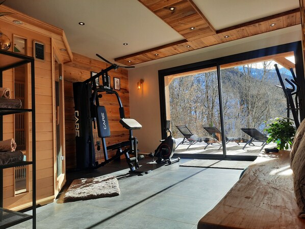 Un gimnasio con equipo de ejercicio, una banca y un ventanal con vistas a árboles.