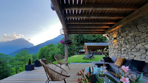 Une terrasse en bois avec des chaises en osier, un canapé et un mur en pierre.