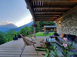 Una terraza de madera con sillas de mimbre, un sofá y una pared de piedra.