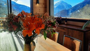 Un intérieur en bois avec une table agrémentée d’un vase de fleurs, de grandes fenêtres offrant une vue sur les montagnes et un plafond en bois.