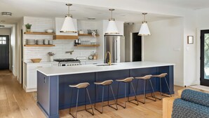 A modern kitchen with a central island, bar stools, white cabinetry, and pendant lighting.