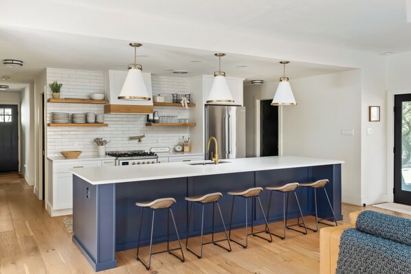 A modern kitchen with a central island, bar stools, white cabinetry, and pendant lighting.
