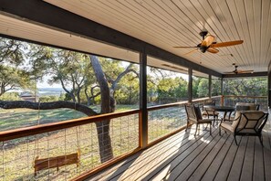 Enjoy the serene views from this outdoor deck, featuring a table and chairs, ceiling fans, and a tree-lined backdrop.