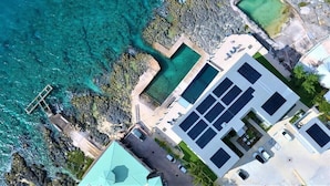 Vista aérea de una propiedad costera con piscina, muelle y un edificio con paneles solares.