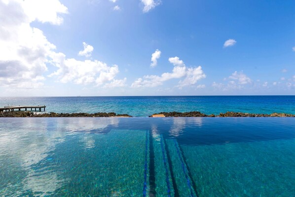 A clear blue pool with a wooden deck extending into the ocean, surrounded by rocky formations.