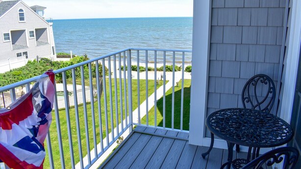 A balcony with a view of the sea, a flag, and a metal table. - Brand new Ocean View Condo with private balcony, steps from the beach! (Dennis Port)