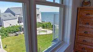 A room with a large window overlooking a grassy yard and a body of water. - Brand new Ocean View Condo with private balcony, steps from the beach! (Dennis Port)