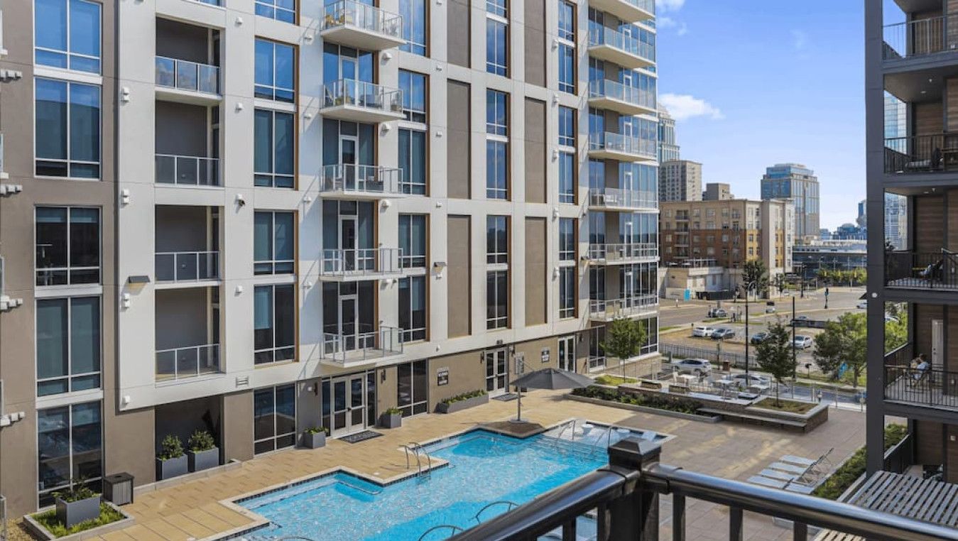 A modern apartment building with a rooftop pool area, multiple balconies, and a view of the cityscape.