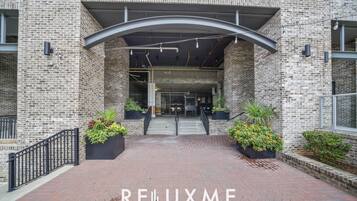 A brick building entrance with a covered walkway, potted plants, and a sign reading "RELLUXME".